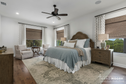 a primary bedroom with a two chairs, hardwood floors and large windows.