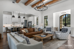 a large custom home with an open floor plan of the kitchen and living room with hardwood floors and vaulted ceilings with wood beams.