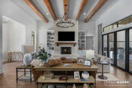 a living room with a fireplace, wood beams, and a larger glass slider to the outdoor kitchen.
