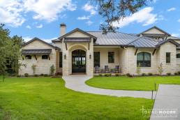 a large custom home with a colored metal roof, black windows, stone, and stucco facade.