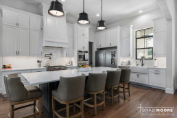 a large kitchen with white cabinets, large island with plenty of seating, lots of lighting, and hardwood floors.