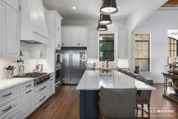 a large custom home with an open floor plan of the kitchen and living room with hardwood floors and vaulted ceilings with wood beams.