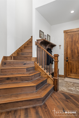 a custom home with wooden stairs, wood flooring and a mud bench