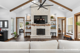 a living room with a large rock fireplace wood beams and a ceiling fan