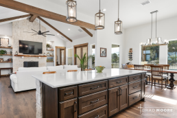 a kitchen with a center island with an open floor concept looking into the family room and wooden beams
